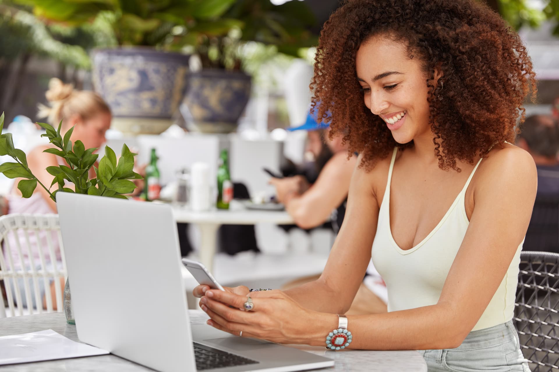 A happy woman shopping online in a café, using both her phone and laptop