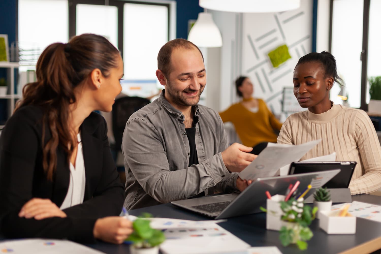 Smiling, diverse business team reviewing and discussing reports at a meeting, with charts and documents spread on the table