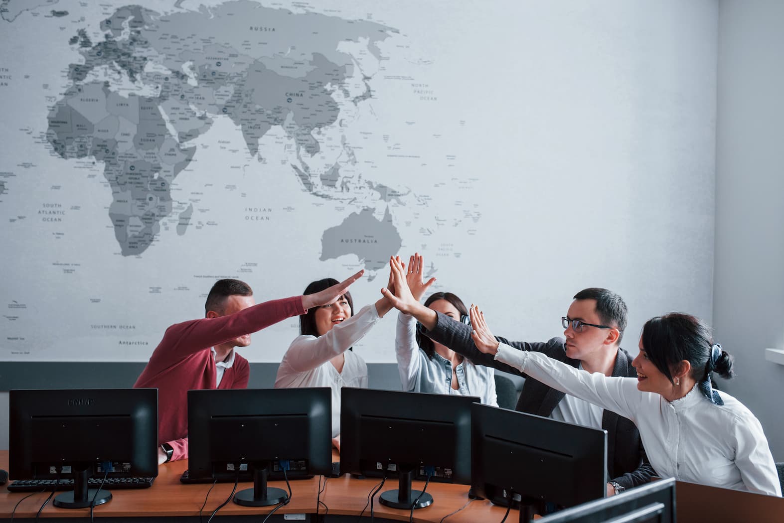 A diverse team celebrating with a high-five in front of a world map, highlighting their success in delivering global solutions