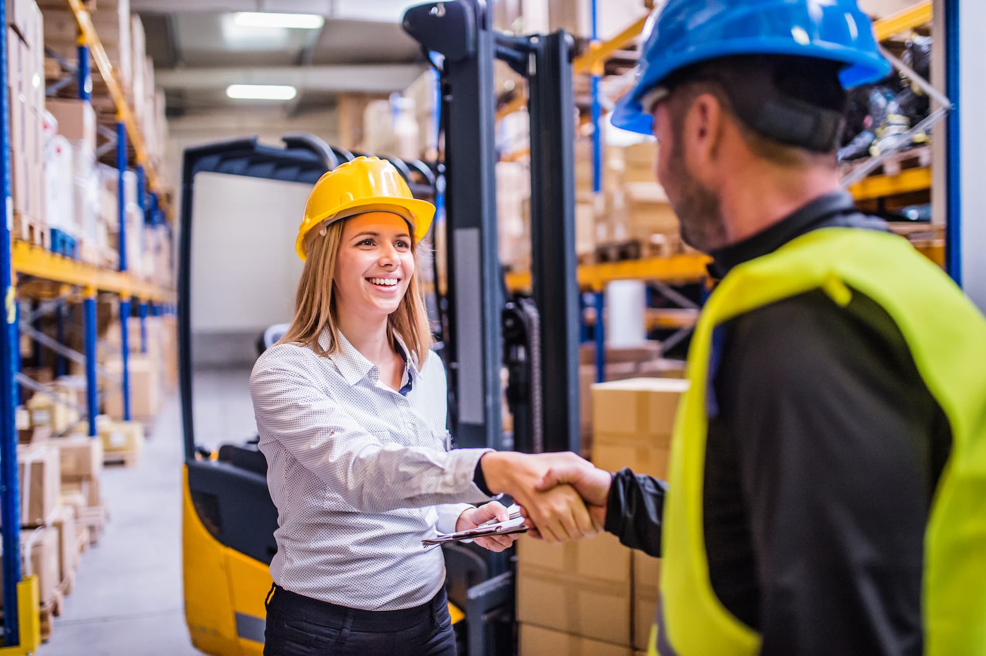 Two business leaders shaking hands in a large logistics warehouse, symbolizing a successful partnership